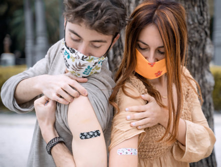 Young couple looking at band-aids on their shoulders after being vaccinated