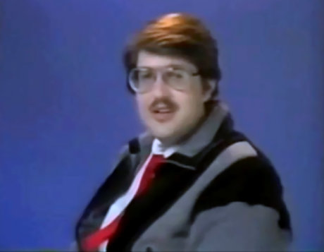 Chubby man with mustache wearing outdoor jacket and red tie in 1980s video dating profile