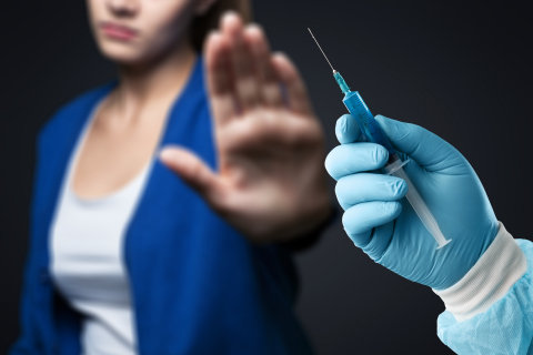 Woman with raised hand refusing syringe held in a doctor's gloved hand